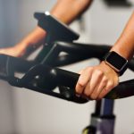 Hands of a woman training at a gym doing spinning or cyclo indoor with smart watch. Sports and fitness concept.